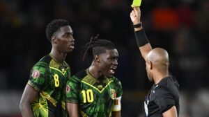 Referee shows a yellow card to a Mali player during a tense moment, with teammates reacting in vibrant green and yellow kits.
