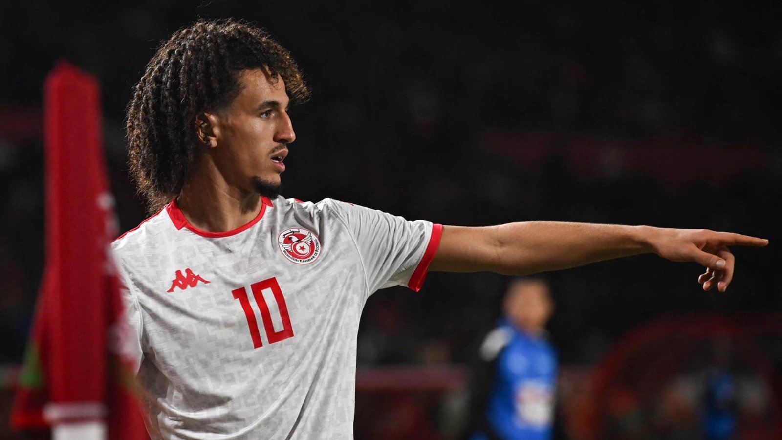 Tunisia's player, wearing a white kit with red accents and the number 10, gestures actively during a match, with fans in the background.