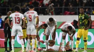 Tunisia players Sassi and Mastouri attend to an injured teammate during a match against Mali, while the referee and opposing players observe.
