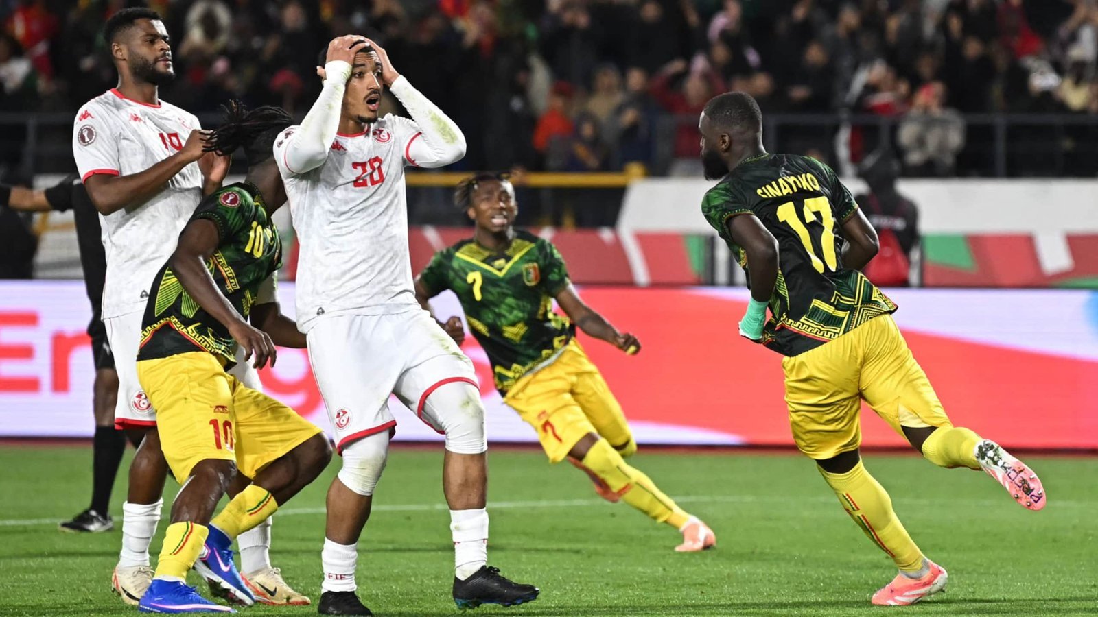 Tunisian players react in disbelief as Guinea celebrates a crucial goal during a tense African Cup of Nations match.