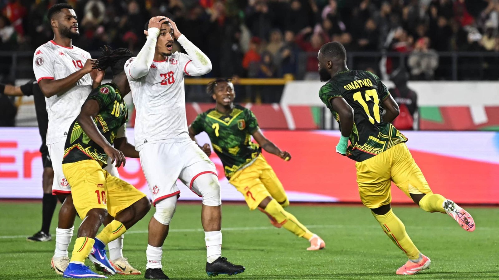 Spelers van Tunesië en Guinee zijn verwikkeld in een gespannen moment tijdens hun wedstrijd, met vieringen van Guinee's Enayko na een doelpunt.