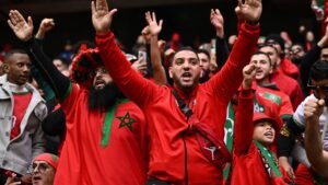 Moroccan fans in vibrant red clothing cheer passionately, showcasing their excitement and national pride in a football match setting.