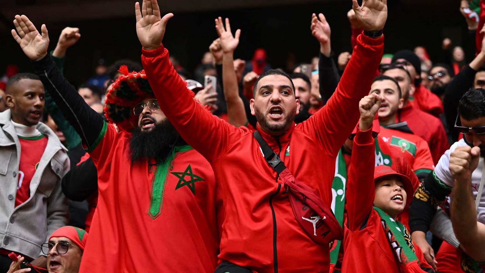 Moroccan fans in vibrant red clothing cheer passionately, showcasing their excitement and national pride in a football match setting.