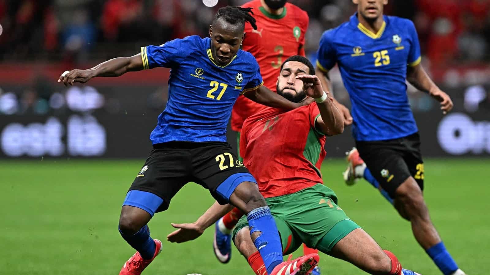 Moroccan player Hakim Ziyech tackles Tanzanian forward Farouk Shikalo during a match, showcasing intense competition in red and blue kits.