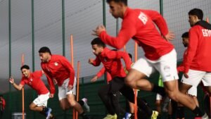Egyptian footballers in red training kits sprint during a training session, showcasing their focus and agility on the pitch.