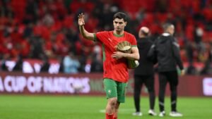 Moroccan player waves to fans while exiting the pitch, wearing a vibrant red and green kit, celebrating a notable moment in the match.