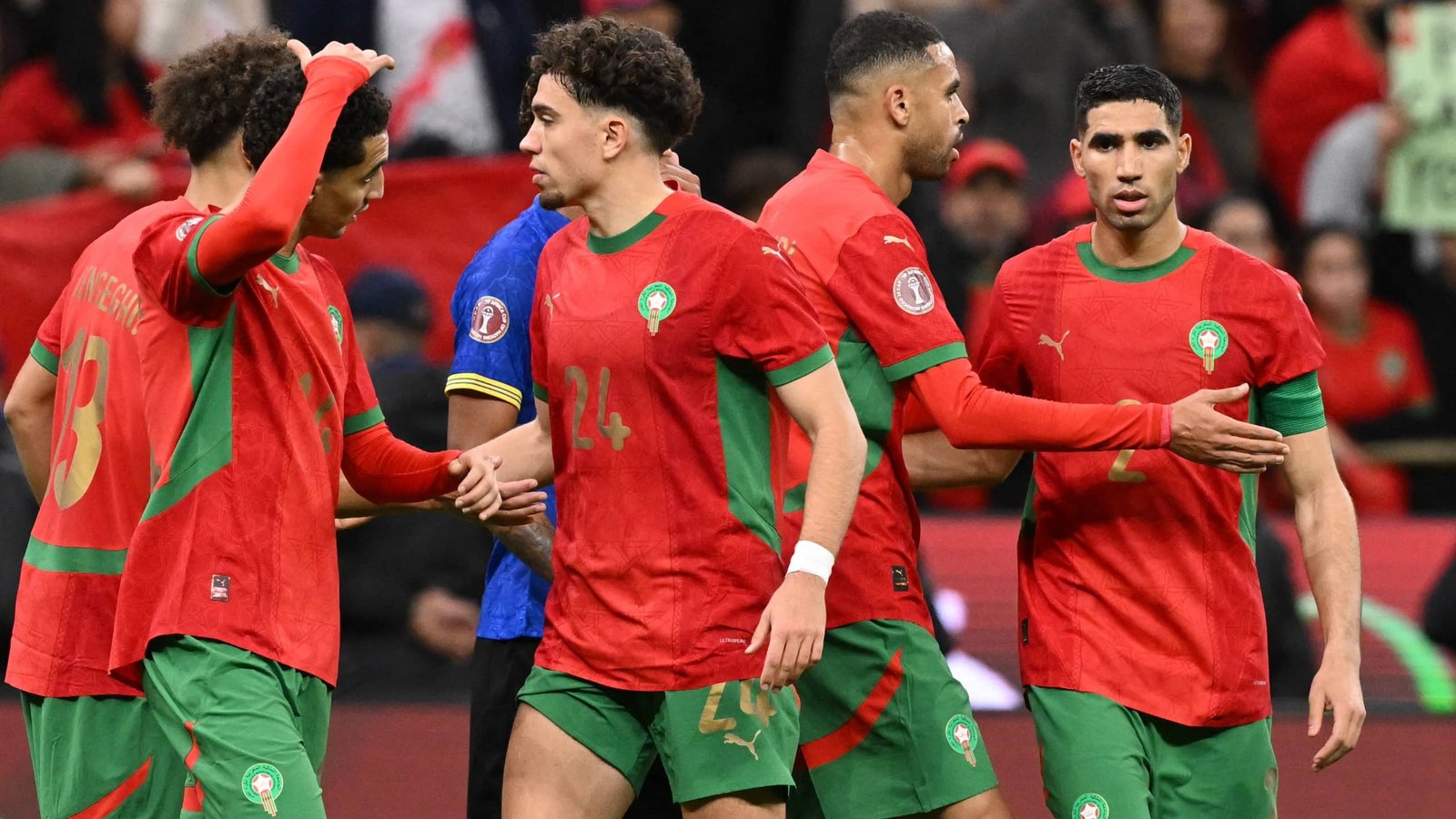 Morocco players celebrate on the pitch, dressed in their red and green kits, showcasing team spirit during a match.