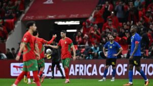 Morocco players celebrate during an Africa Cup of Nations match, with fans in red behind them and opposing team in blue.