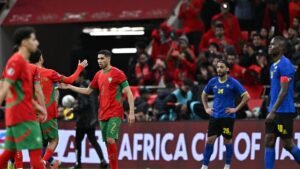 Morocco players celebrate a goal during the Africa Cup of Nations match, with fans in vibrant red in the background.