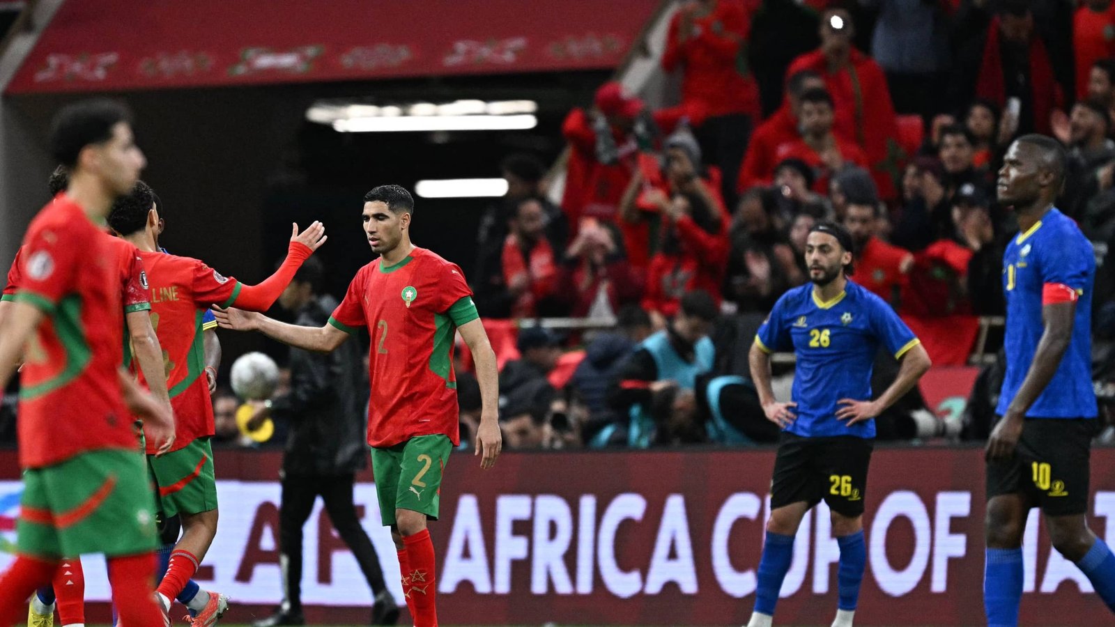 Morocco players celebrate a goal during the Africa Cup of Nations match, with fans in vibrant red in the background.