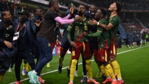 Les joueurs camerounais célèbrent avec passion après un but crucial, portant des tenues vert et rouge vifs, dans une atmosphère festive sur le terrain.