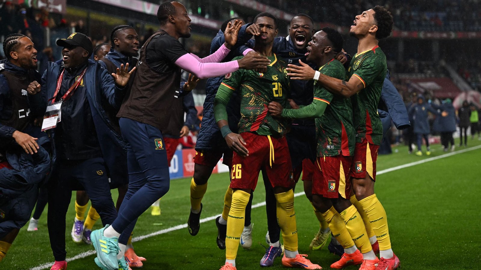 Les joueurs camerounais célèbrent avec passion après un but crucial, portant des tenues vert et rouge vifs, dans une atmosphère festive sur le terrain.