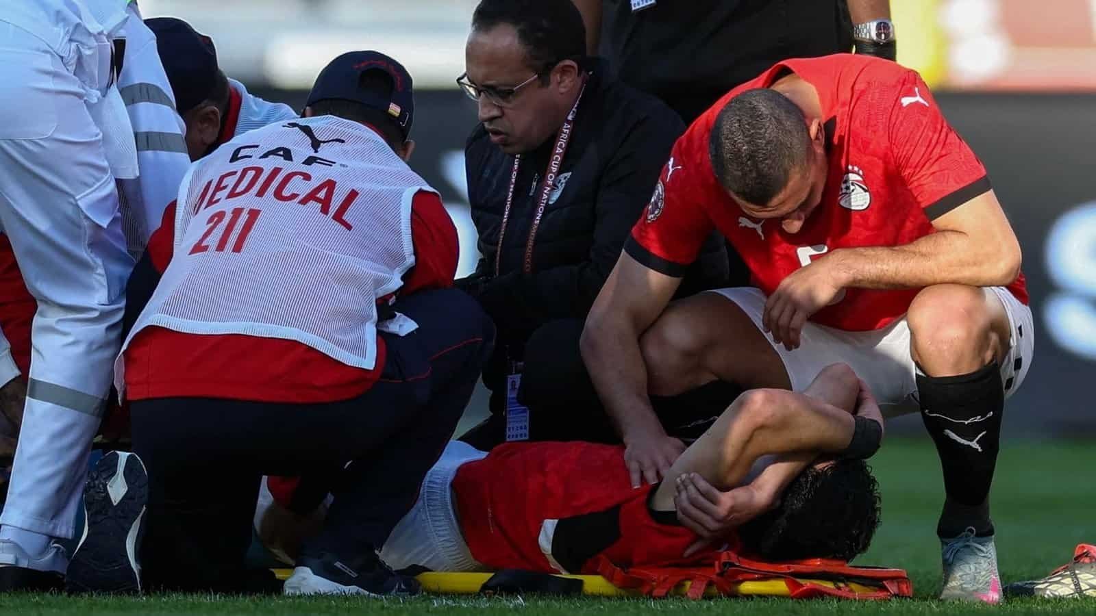Les joueurs égyptiens et le personnel médical portent secours à un coéquipier blessé sur le terrain, illustrant un moment d'inquiétude pendant le match.