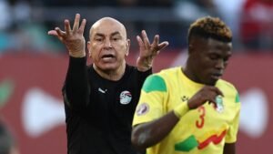 L'entraîneur égyptien gesticulant avec animation pendant un match, tandis qu'un joueur malien en tenue jaune reste concentré sur le jeu.