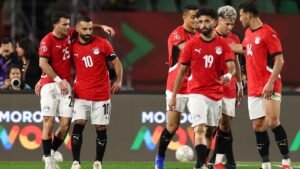 Les joueurs égyptiens célèbrent pendant un match, portant des maillots rouges avec des shorts blancs, montrant la camaraderie d'équipe sur le terrain.