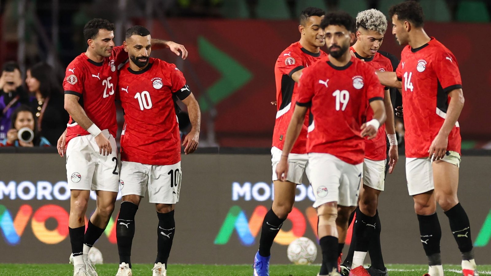 Les joueurs égyptiens célèbrent pendant un match, portant des maillots rouges avec des shorts blancs, montrant la camaraderie d'équipe sur le terrain.
