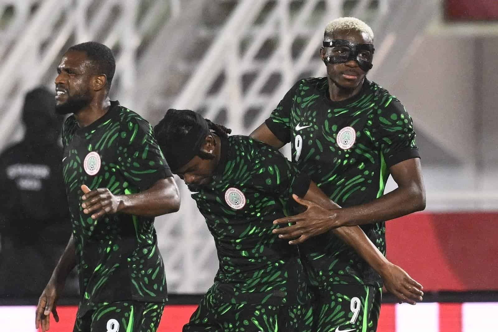 Les joueurs nigérians célèbrent un but, portant des maillots verts vifs avec un motif unique. Un joueur porte un masque de protection, renforçant l'excitation de la scène.