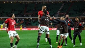 Egyptische spelers die gepassioneerd feestvieren op het veld, gekleed in rode en zwarte tenues, na een succesvolle wedstrijd, tegen een levendige stadionachtergrond.