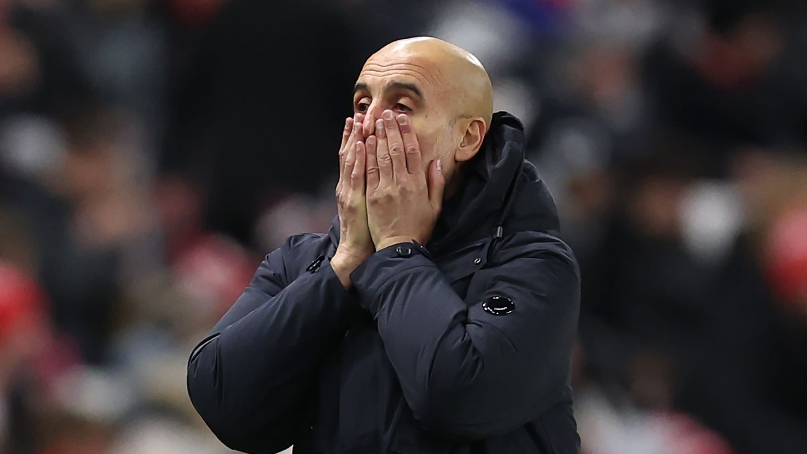 Concerned manager with hands on face, wearing a dark jacket, displaying deep emotion during an intense match scenario.