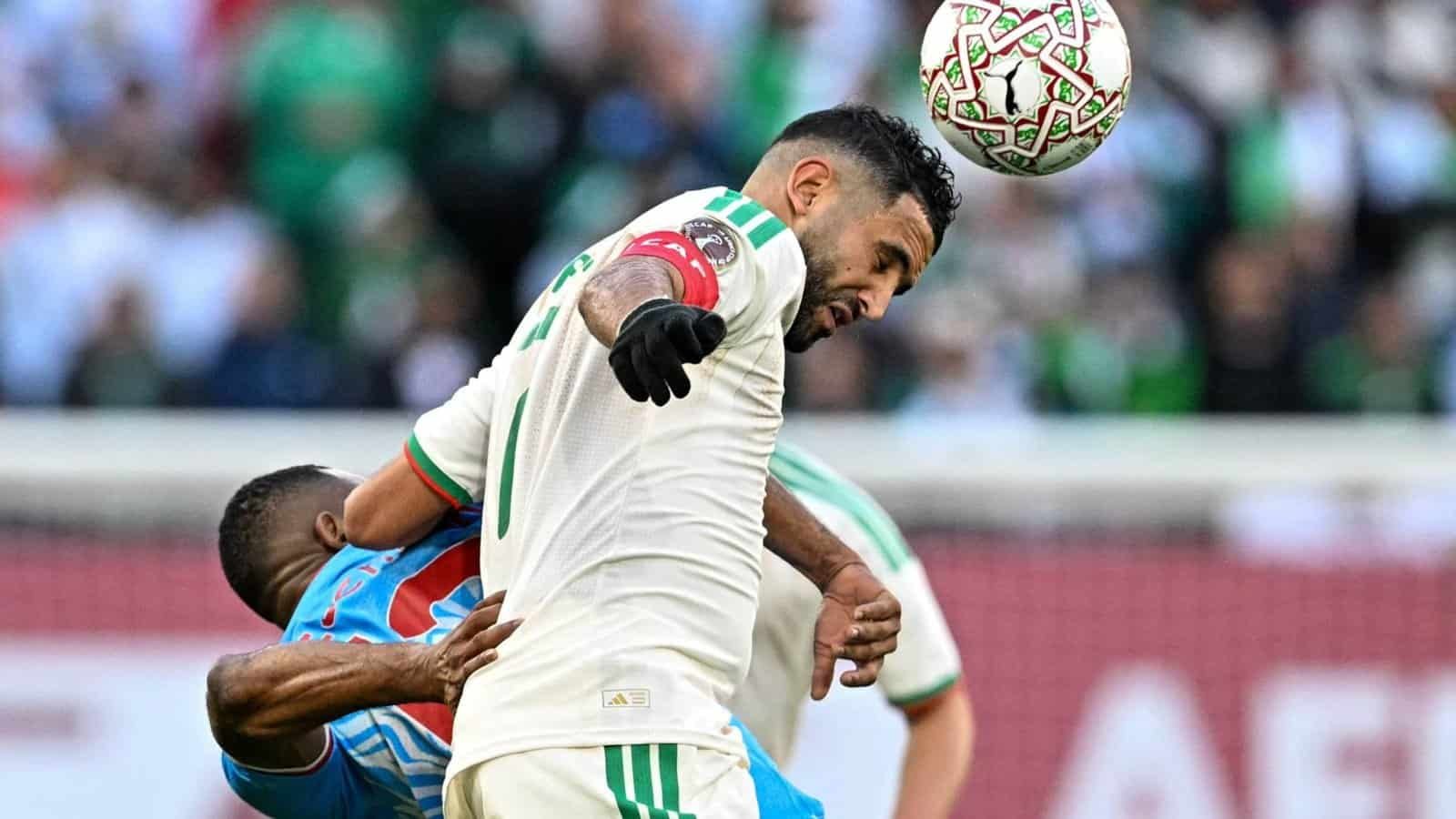 Riyad Mahrez de l'Algérie se bat pour le ballon contre un adversaire lors d'un moment intense d'un match de la CAN, illustrant une compétition acharnée.