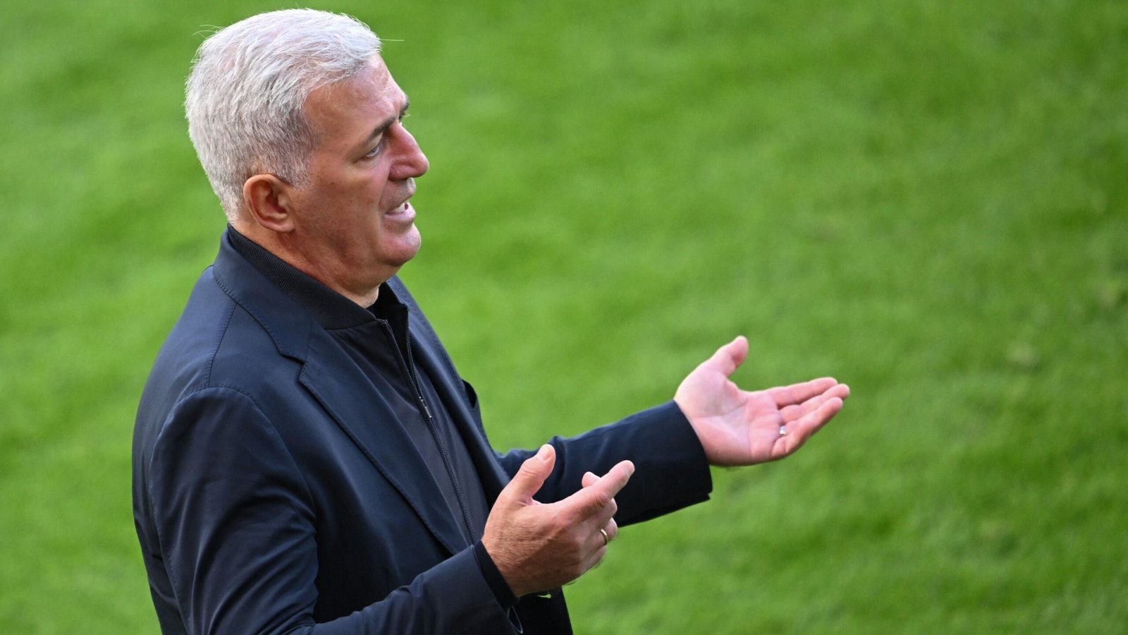 L'entraîneur gesticulant avec passion en bord de terrain, vêtu de noir sur un terrain d'un vert éclatant, transmettant une intense détermination pendant un match.