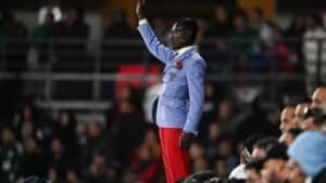 A passionately dressed fan in a light blue suit and red trousers stands out amongst the crowd, waving enthusiastically during the match.