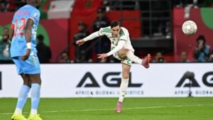 Le joueur marocain n°22 exécute une frappe remarquable lors d'un match contre un adversaire vêtu de bleu, avec des drapeaux nationaux en arrière-plan.