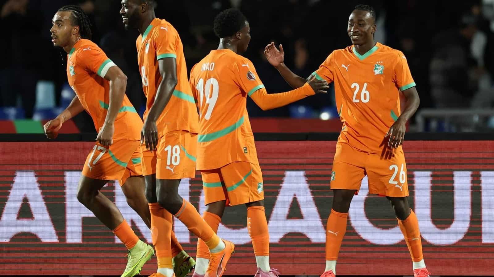 Ivorian players celebrate in their vibrant orange kits during the Africa Cup, showcasing camaraderie and excitement on the pitch.