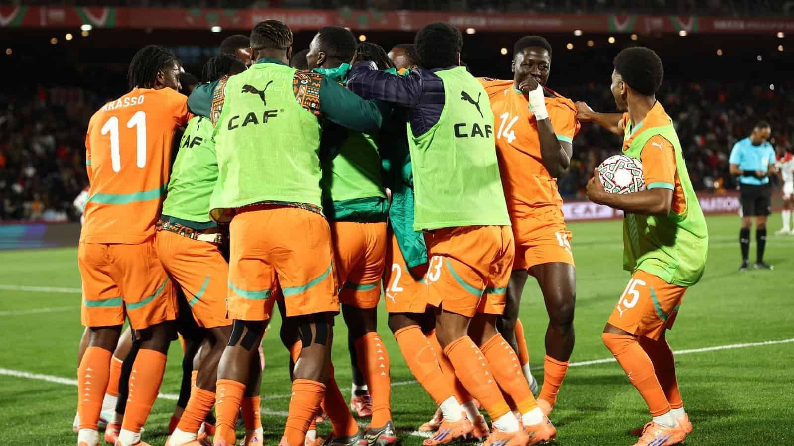 L'équipe de football marocaine célébrant la victoire sur le terrain dans des maillots orange vifs.