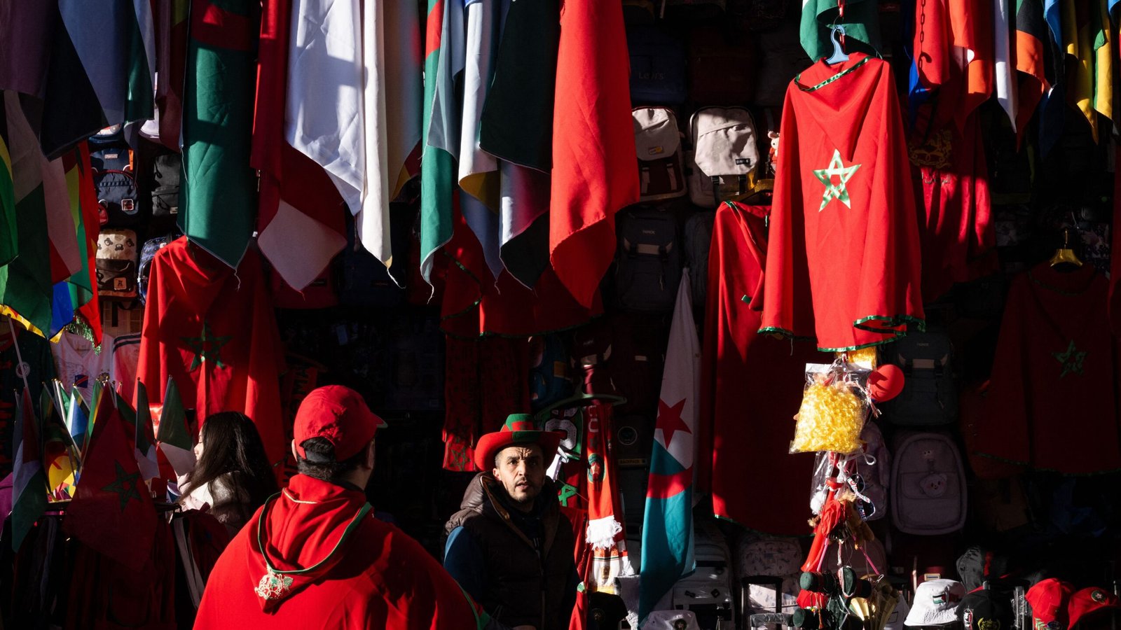Moroccan fans in red attire showcase national pride amidst a vibrant display of flags and merchandise in a bustling market setting.