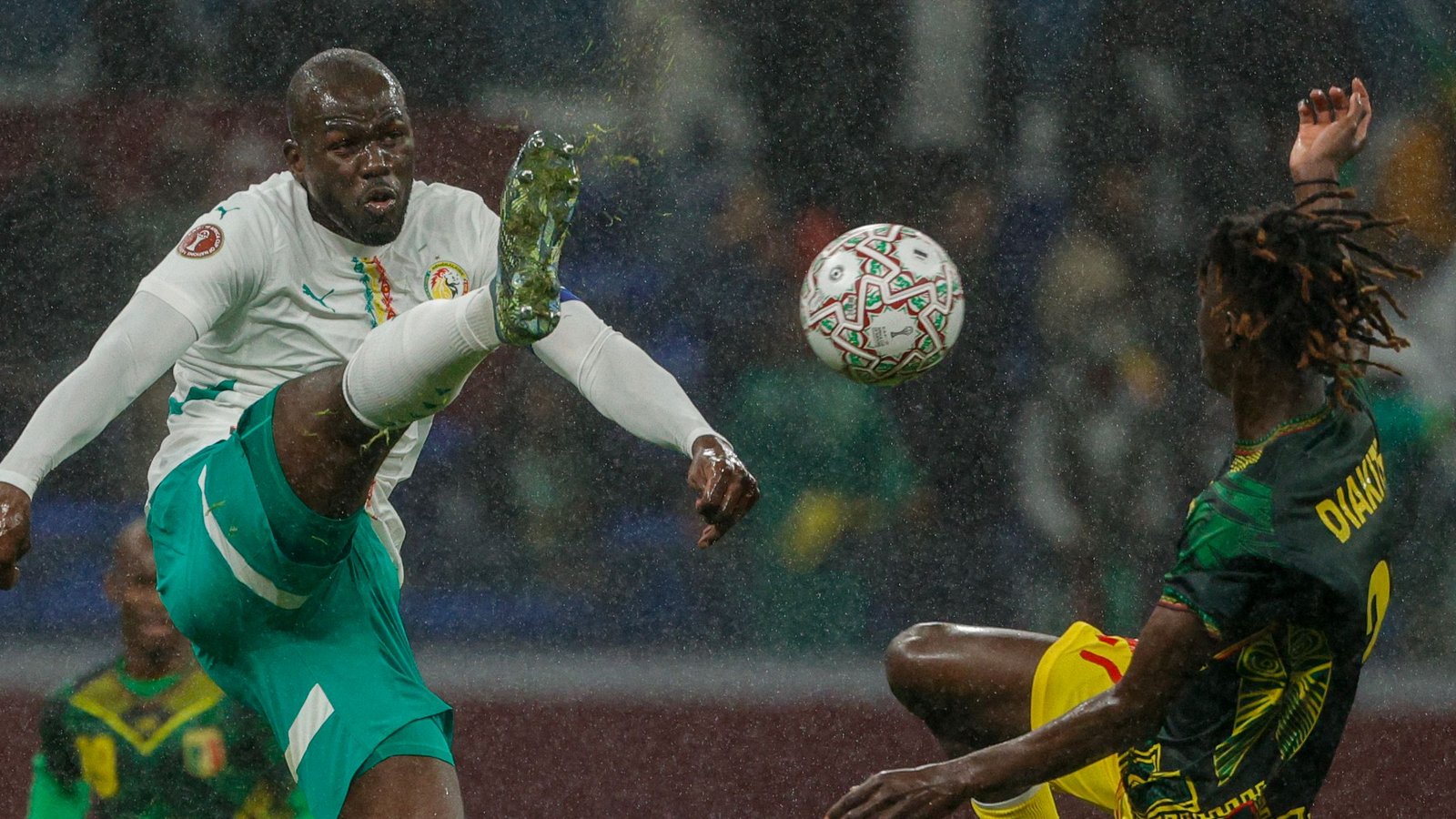 Senegalese player strikes the ball mid-air in a rainy match against Cameroon, showcasing action and intensity on the pitch.