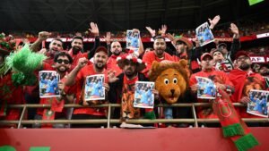Les supporters marocains célèbrent, vêtus de rouge et de vert vibrants, en brandissant des photos et en encourageant avec passion pendant un match, démontrant ainsi leur esprit d'équipe.