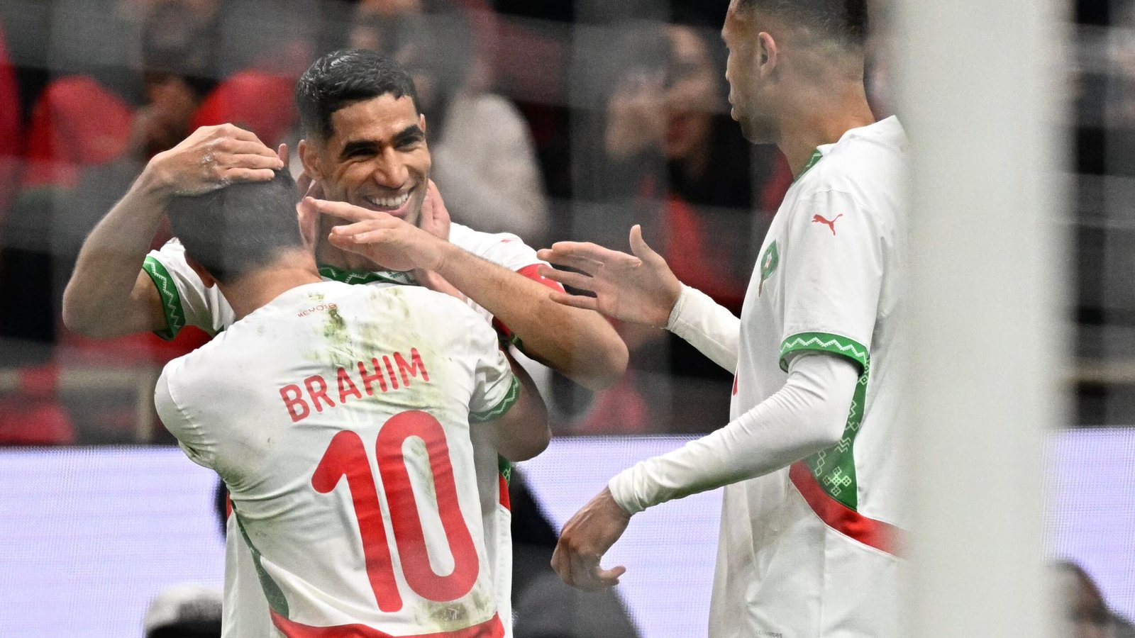 Moroccan players celebrate a goal, featuring Brahim in a stained jersey marked with the number 10, vibrant red and green team colours in focus.