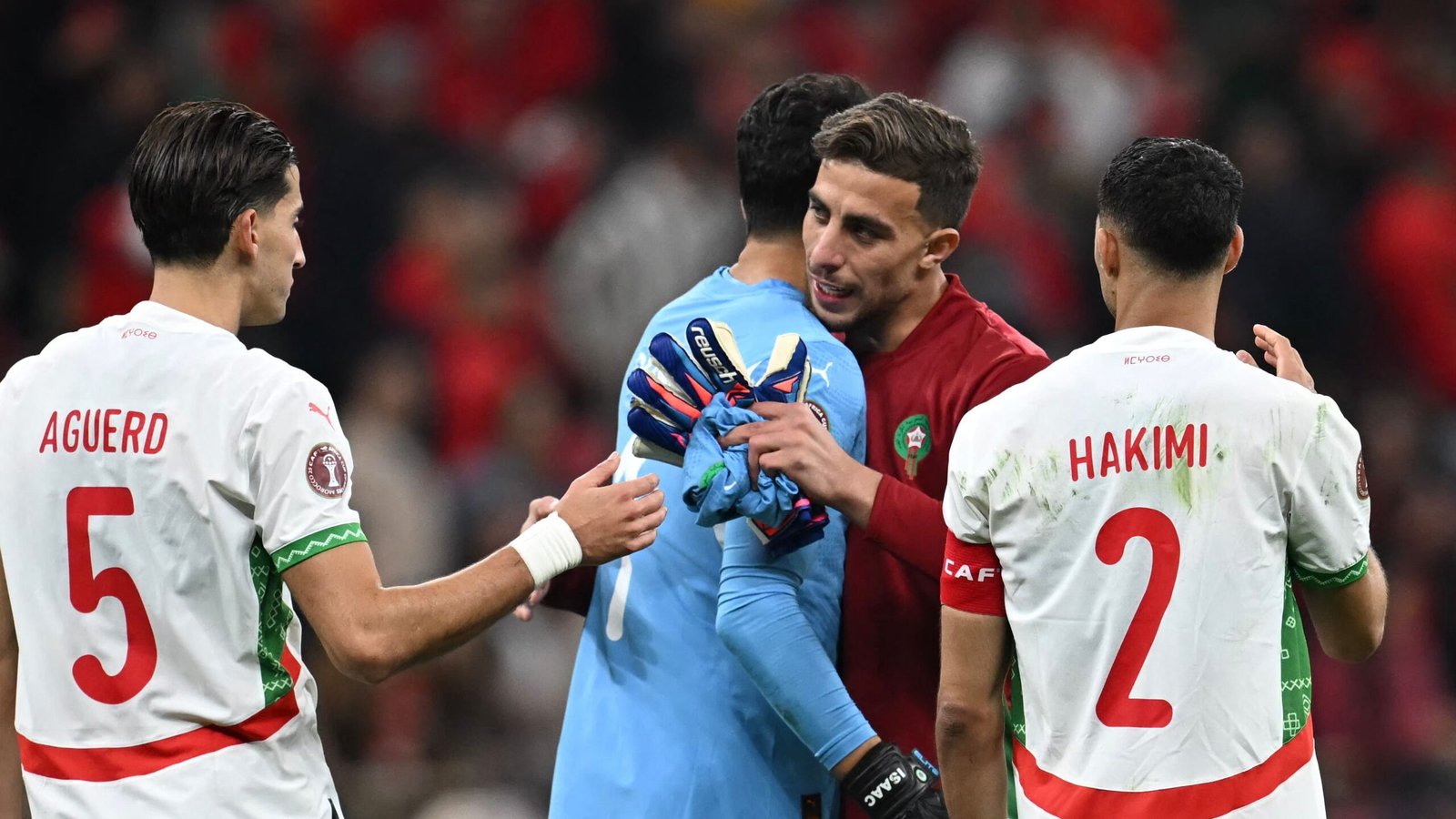 Les joueurs marocains Aguerd, Hakimi et leur gardien partagent un moment après le match en maillots rouges et blancs, reflétant la camaraderie sur le terrain.