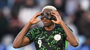 Victor Osimhen du Nigeria ajuste un masque noir pendant un match, portant le maillot vert vif de l'équipe avec des motifs distinctifs.