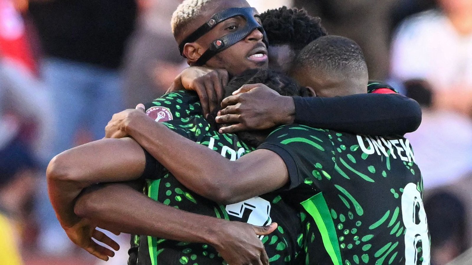 Des joueurs en maillots verts et noirs célèbrent un but, s'enlaçant étroitement avec joie, montrant camaraderie et esprit d'équipe.