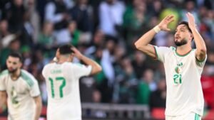 Des joueurs algériens montrant de la frustration pendant un match, avec le joueur 21 se tenant la tête et le joueur 17 regardant, sur fond de fans.