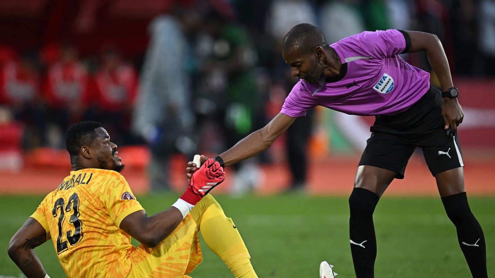 Le gardien de but Yassine Bounou, en tenue jaune, reçoit de l'aide d'un arbitre en rose lors d'un match tendu de la CAN.