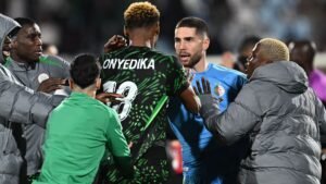 Interaction tendue entre joueurs pendant un match, avec Onyedikah en maillot à motifs et un gardien de but en bleu. Les émotions intenses sont perceptibles.