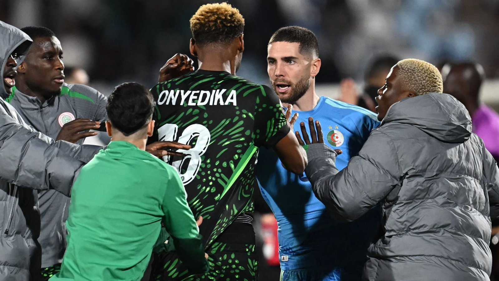 Interaction tendue entre joueurs pendant un match, avec Onyedikah en maillot à motifs et un gardien de but en bleu. Les émotions intenses sont perceptibles.