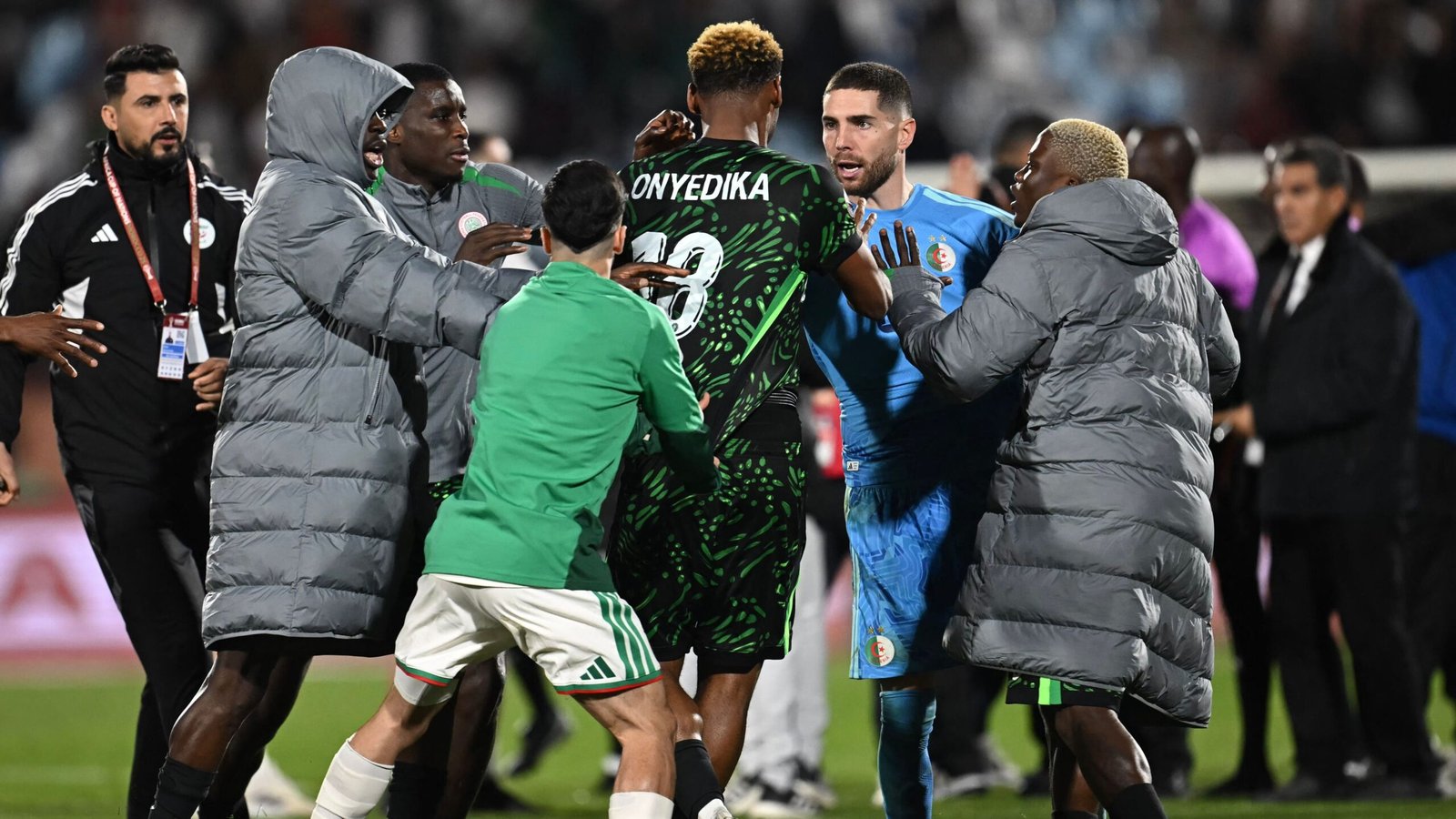 Les joueurs du Nigeria et de l'Algérie se confrontent après le match, montrant une forte tension. Des maillots verts et noirs notables sont présents.