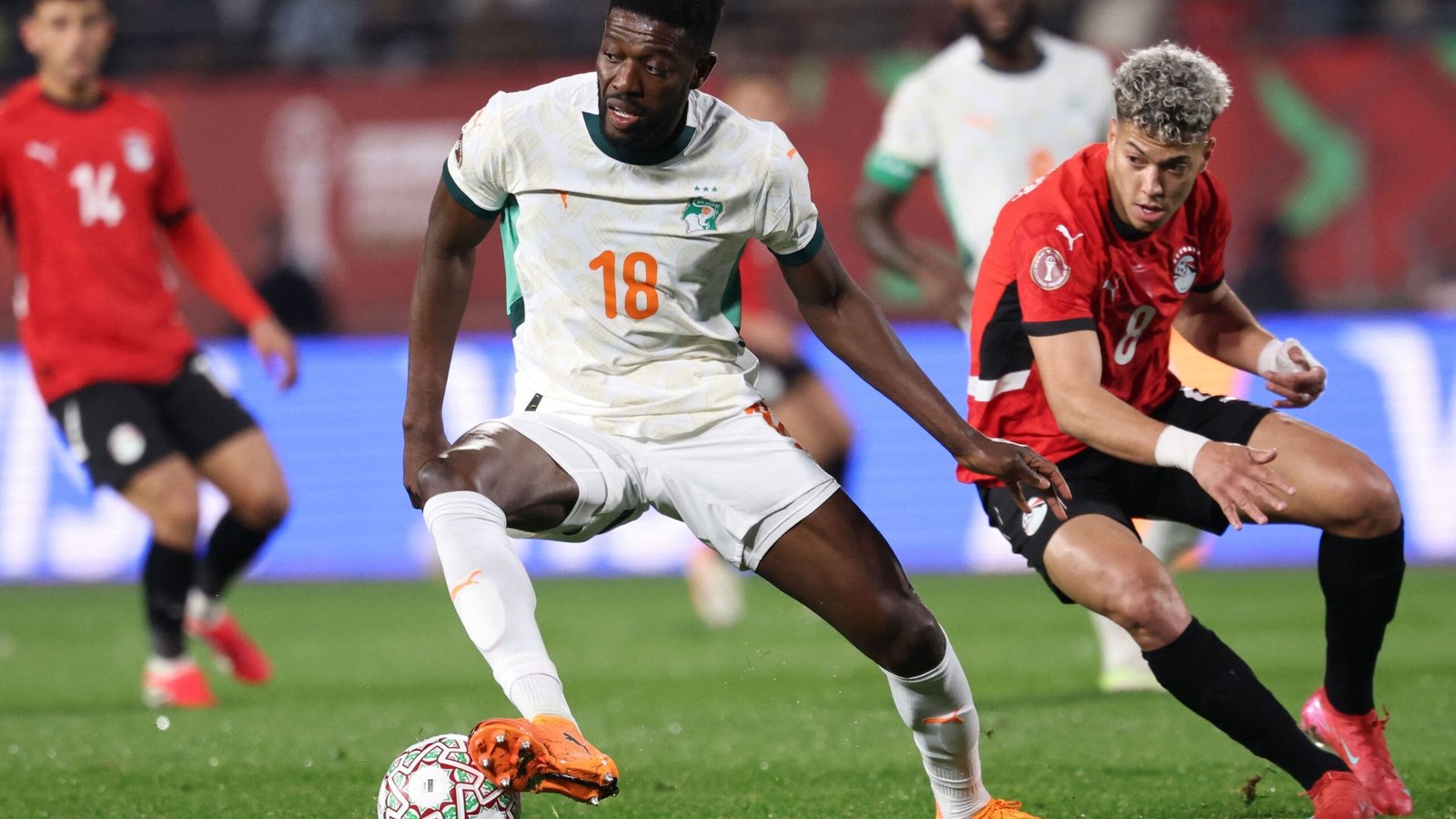 Ivory Coast player in white, number 18, controls the ball against Egypt's number 8 during a tense AFCON match, showcasing dynamic action.