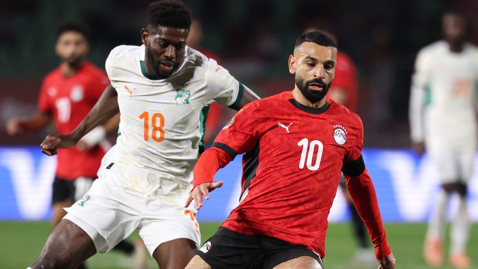 Mohamed Salah in Egypt's red kit, evading an Ivorian defender in light green. Action from a tense international match.