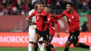 Les joueurs égyptiens célèbrent un but lors du match contre le Sénégal, portant leurs maillots rouges avec excitation dans une atmosphère de stade vibrante.