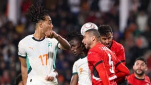 Les joueurs marocains et ivoiriens se disputent le ballon pendant un moment tendu dans un match, montrant des expressions intenses et des couleurs d'équipe vibrantes.
