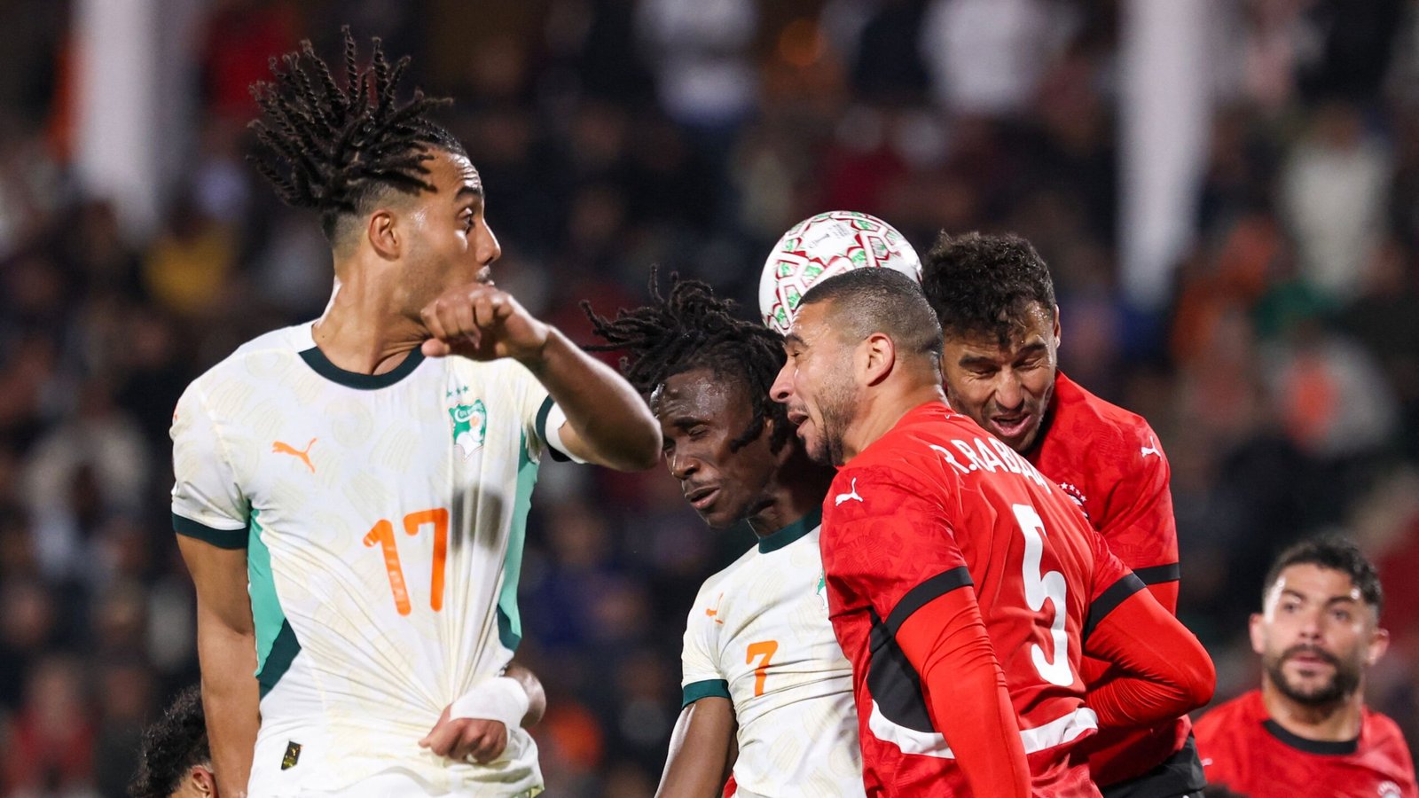 Les joueurs marocains et ivoiriens se disputent le ballon pendant un moment tendu dans un match, montrant des expressions intenses et des couleurs d'équipe vibrantes.
