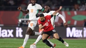 Egypt's number 10 player evades two Ivorian defenders during a tense match, showcasing their competitive spirit in a vibrant stadium.