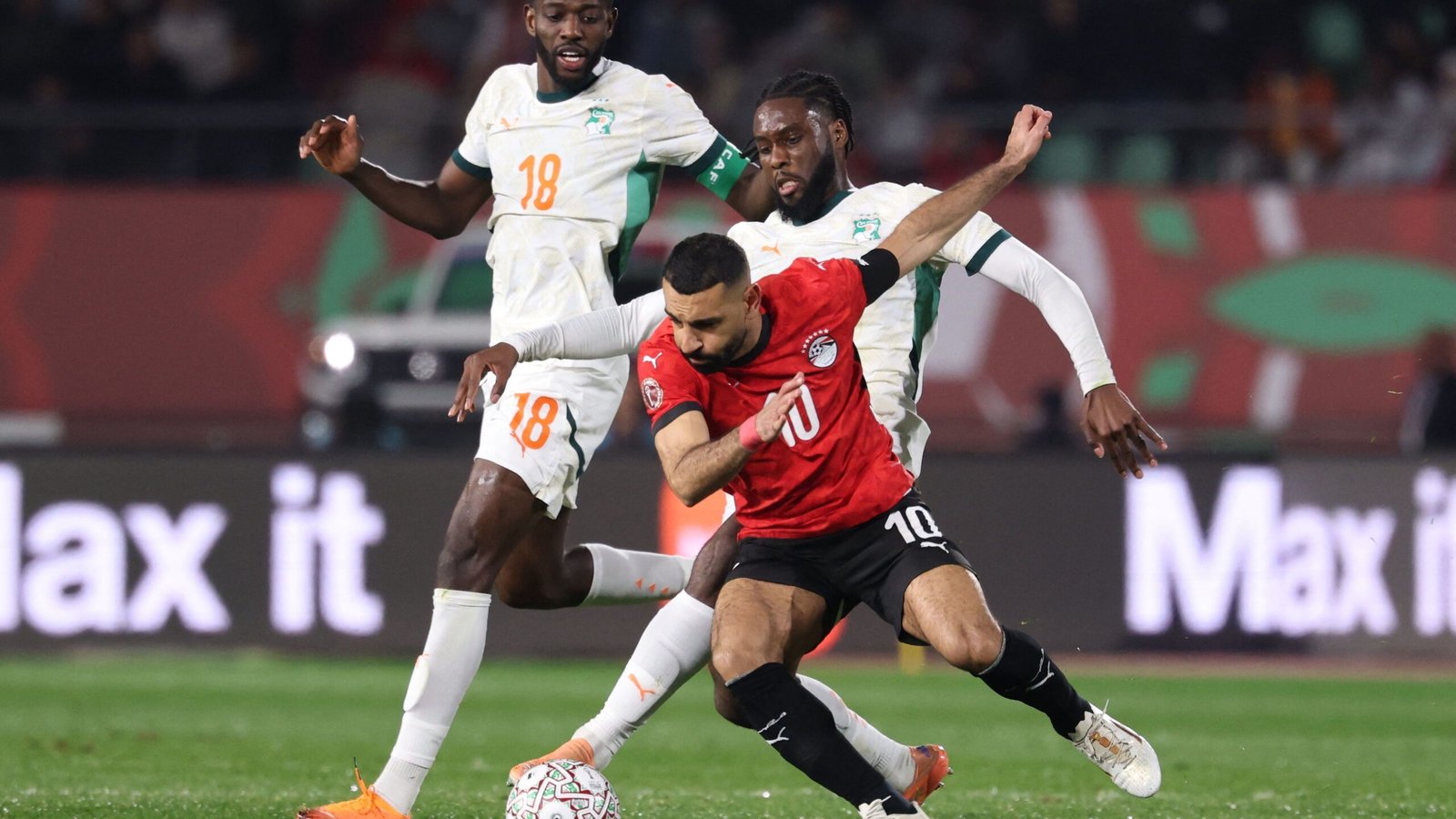Egypt's number 10 player evades two Ivorian defenders during a tense match, showcasing their competitive spirit in a vibrant stadium.