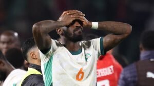 Ivorian player with shirt number 6 holds his head in despair after a match, wearing a white jersey with green accents.
