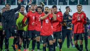 لاعبو كرة القدم المصريون يرتدون القمصان الحمراء يحتفلون بانتصار، ويقود محمد صلاح (10) التصفيق، وسط حشد متحمس.